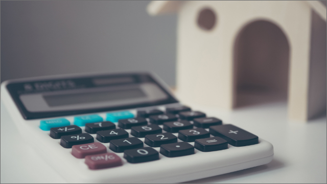 Close up of calculator with a blurred wooden toy house in the background.